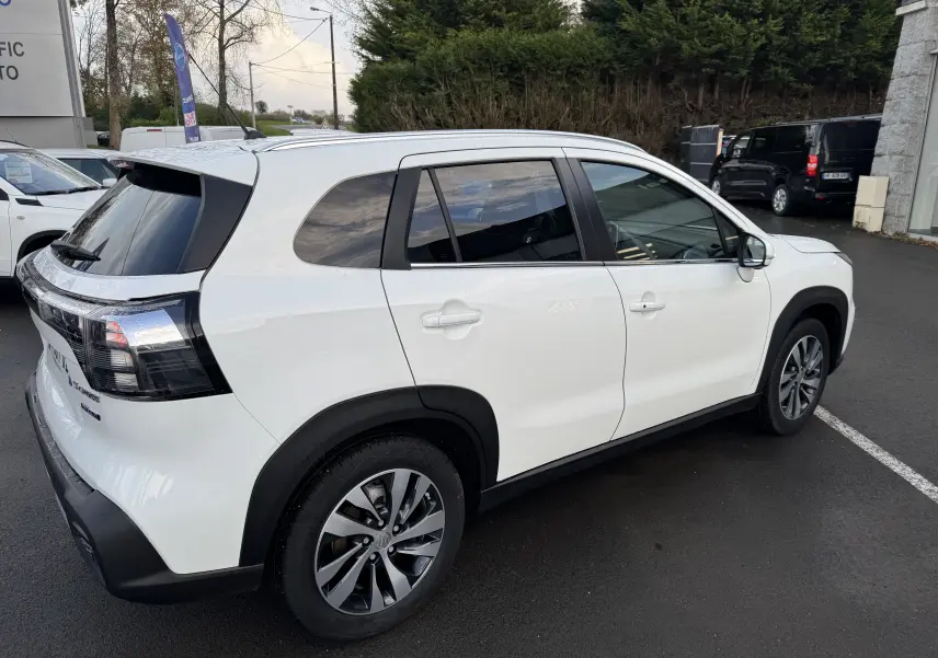 Suzuki S-Cross blanc en vue 3/4 arrière côté droit, avec vitres teintées et jantes alliage distinctives.