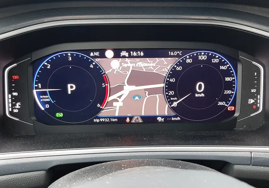 Tableau de bord numérique du Volkswagen T-Roc gris pyrite 2023, affichant la navigation et compteurs à l'arrêt.