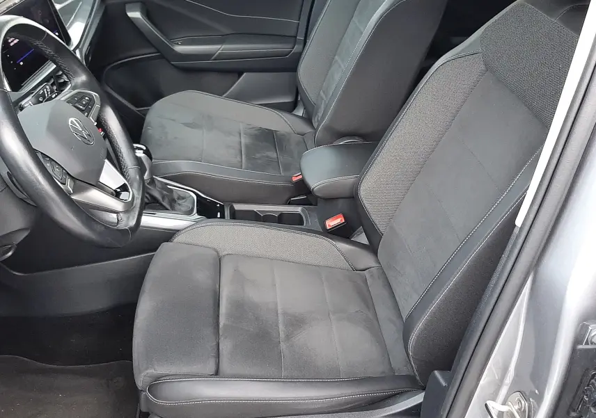 Vue intérieure côté conducteur du Volkswagen T-Roc gris pyrite, montrant les sièges noirs en tissu et alcantara avec console centrale.