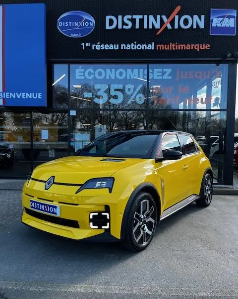 Renault R5 Techno jaune vue 3/4 avant droite, avec phares LED et jantes noires distinctives, devant un showroom Distinxion.