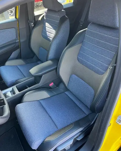 Vue intérieure côté avant droit de la Renault R5 jaune 2024, sièges en tissu bleu avec accoudoir central.