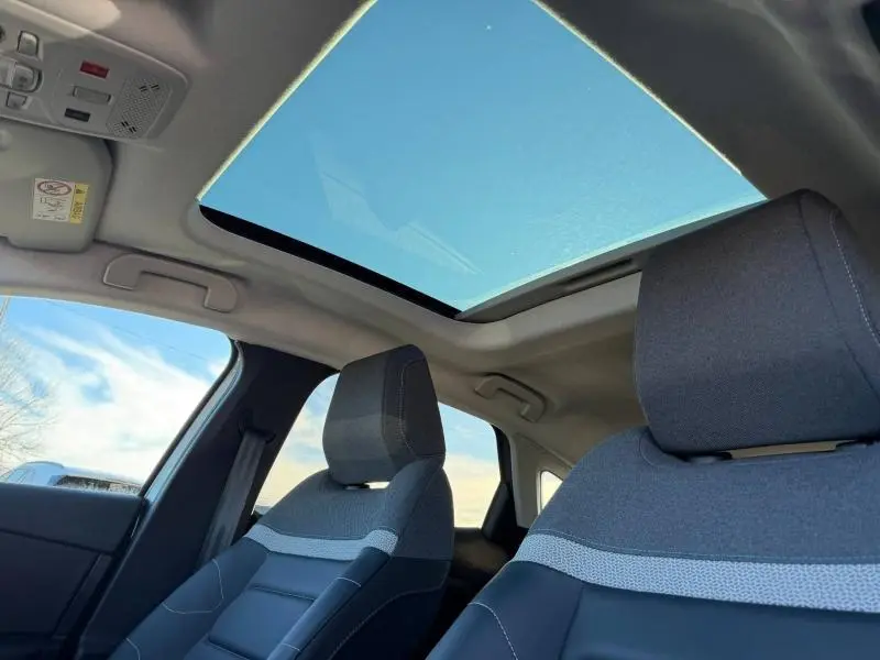 Vue intérieure avant de la Citroën C4 2024 avec toit panoramique et sièges tissu gris à détails contrastés.