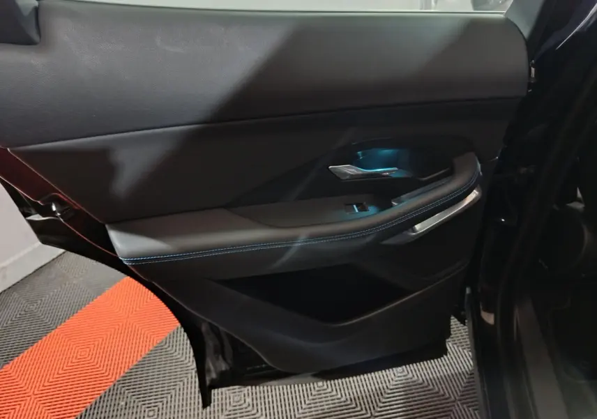 Vue intérieure côté gauche de la porte arrière noire du Jaguar E-PACE avec éclairage bleu et surpiqûres contrastantes.