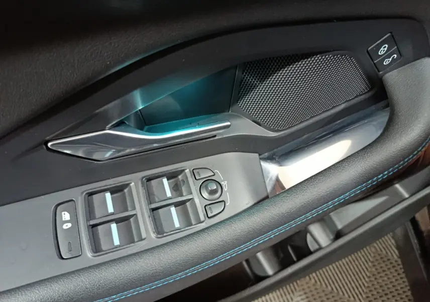 Gros plan sur la commande des vitres côté conducteur du Jaguar E-PACE noir, avec surpiqûres bleues et poignée argentée.