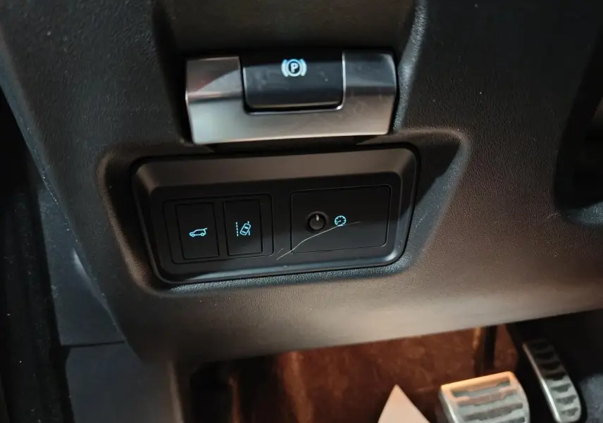 Gros plan sur les commandes sous le volant noir du Jaguar E-PACE P200, avec bouton frein à main électrique et régulateur de vitesse.