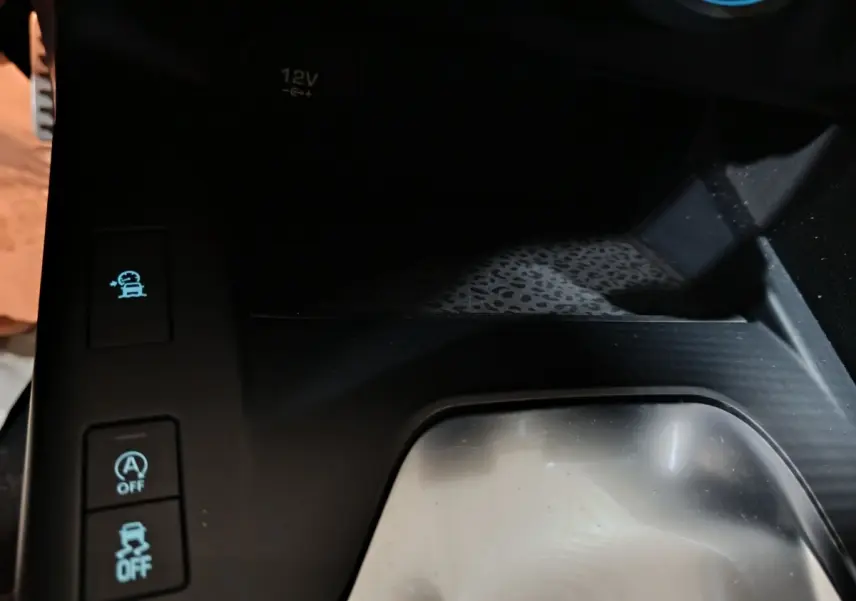 Gros plan sur la console centrale noire du Jaguar E-PACE 2019, avec boutons d’aide à la conduite et prise 12V visible.