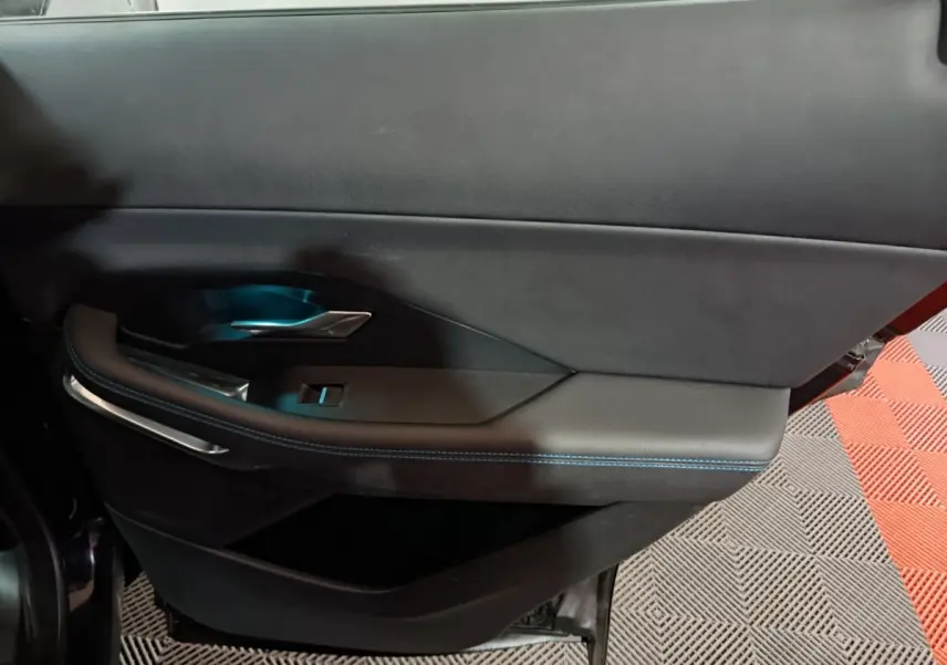 Gros plan sur la porte intérieure côté gauche du Jaguar E-PACE noir, avec surpiqûres bleues et poignée métal.