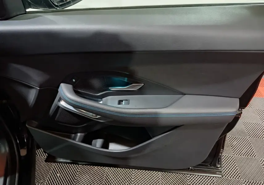 Vue latérale du panneau de porte intérieur noir de la Jaguar E-PACE 2019 avec surpiqûres bleues et poignée argentée.