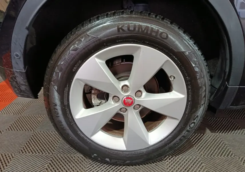 Gros plan sur la roue avant droite d’un Jaguar E-PACE noir, jante alliage argent avec logo Jaguar rouge au centre.