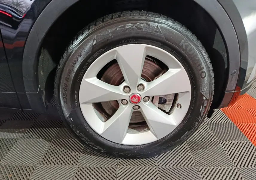 Gros plan sur la roue avant droite noire d’un Jaguar E-PACE 2019 avec jante argentée et logo rouge Jaguar au centre.