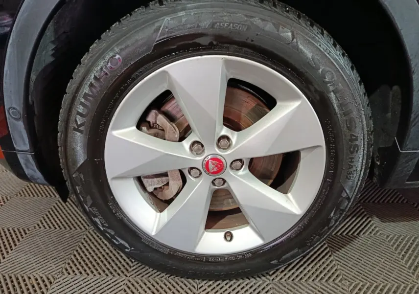 Gros plan sur la roue avant gauche d'une Jaguar E-PACE noire, avec jante argentée et logo Jaguar rouge au centre.