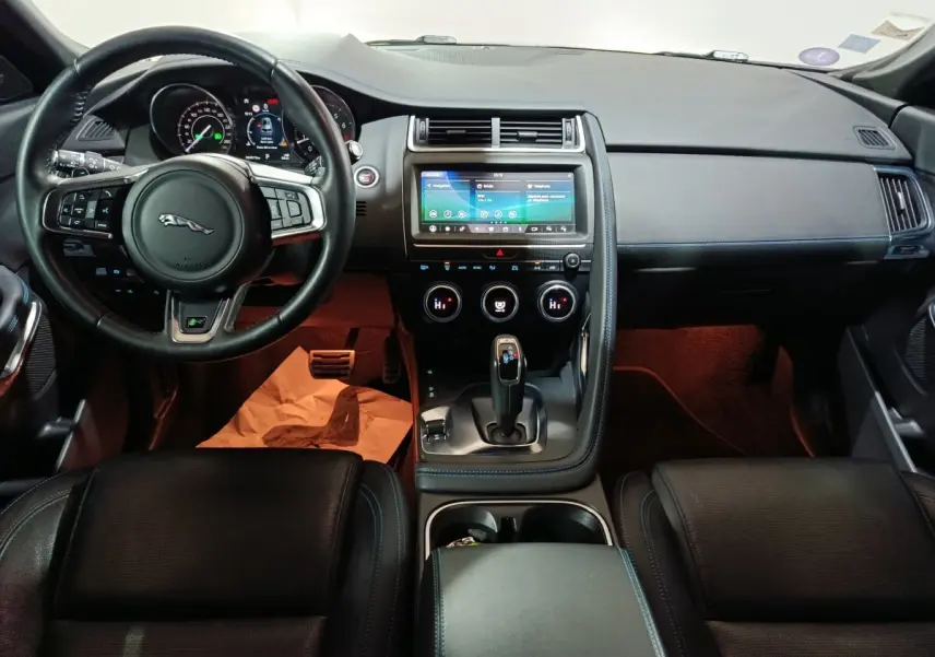 Vue intérieure avant du tableau de bord noir du Jaguar E-PACE 2019 avec écran tactile central et volant cuir multifonctions.