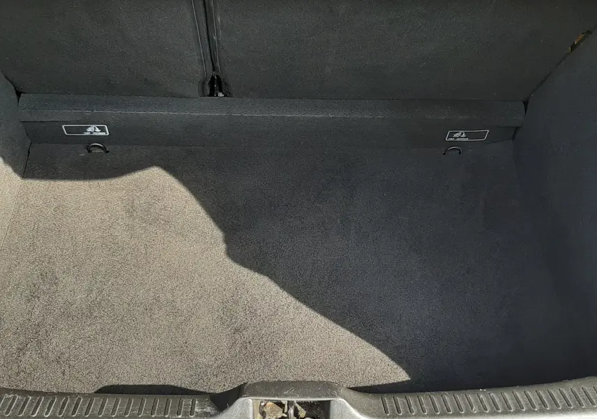 Coffre ouvert vu de dessus, intérieur noir propre avec tapis de sol et crochets de fixation visibles.