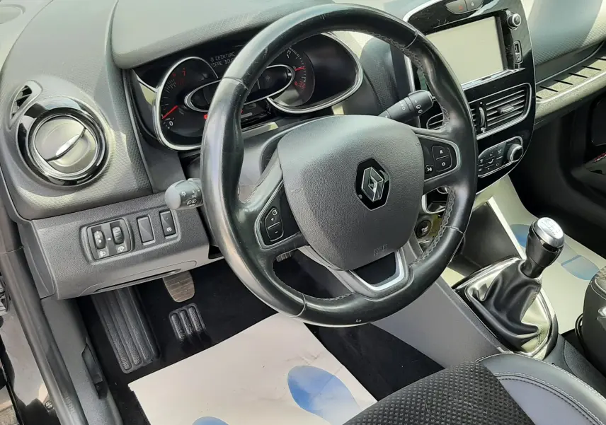 Vue intérieure côté conducteur de la Renault Clio IV noire, volant multifonction et levier de vitesses manuel visibles.