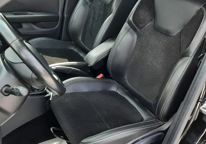 Vue intérieure côté conducteur de la Renault Clio IV noire, mettant en valeur les sièges mixtes cuir et tissu noir avec surpiqûres blanches.