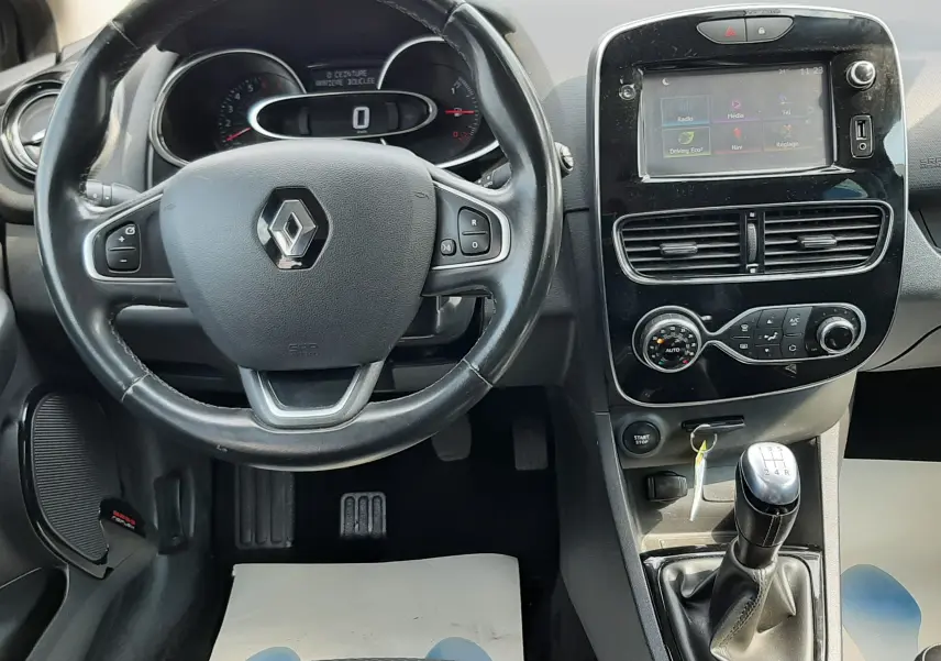Vue intérieure avant centrée sur le volant noir Renault, tableau de bord digital et console centrale avec écran tactile et levier de vitesse manuel.
