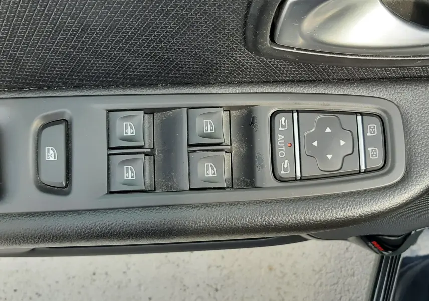 Vue rapprochée des commandes de lève-vitres et réglages des rétroviseurs sur la porte côté conducteur d'une Renault Clio IV noire.
