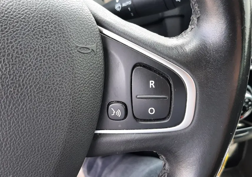 Gros plan sur le volant noir de la Renault Clio IV 2018, avec commandes vocales et boutons R et O visibles.