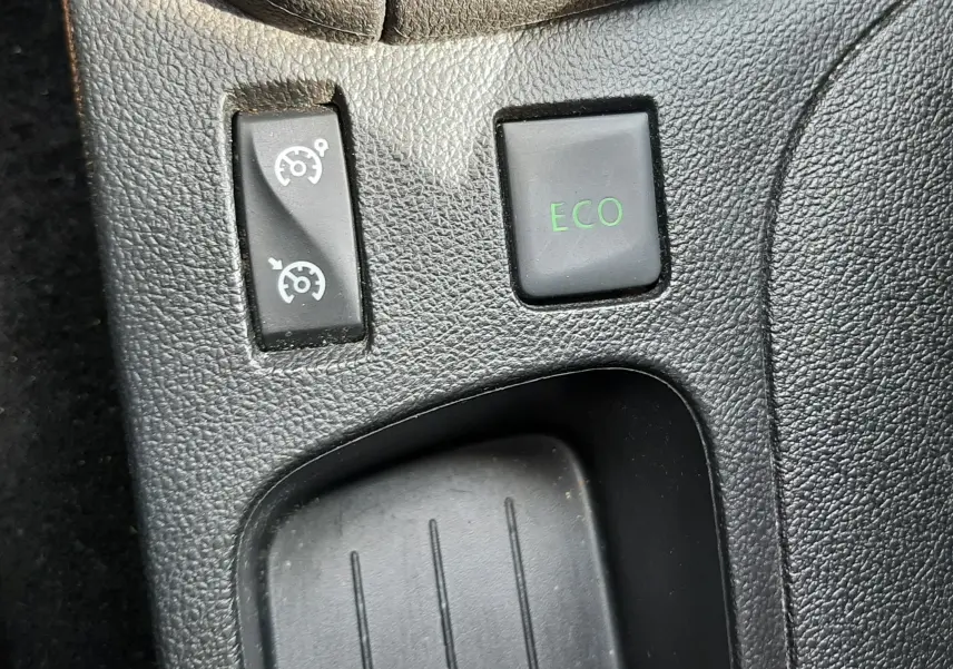 Gros plan sur les boutons de commande du mode ECO et du régulateur de vitesse dans l'habitacle d'une Renault Clio IV noire.