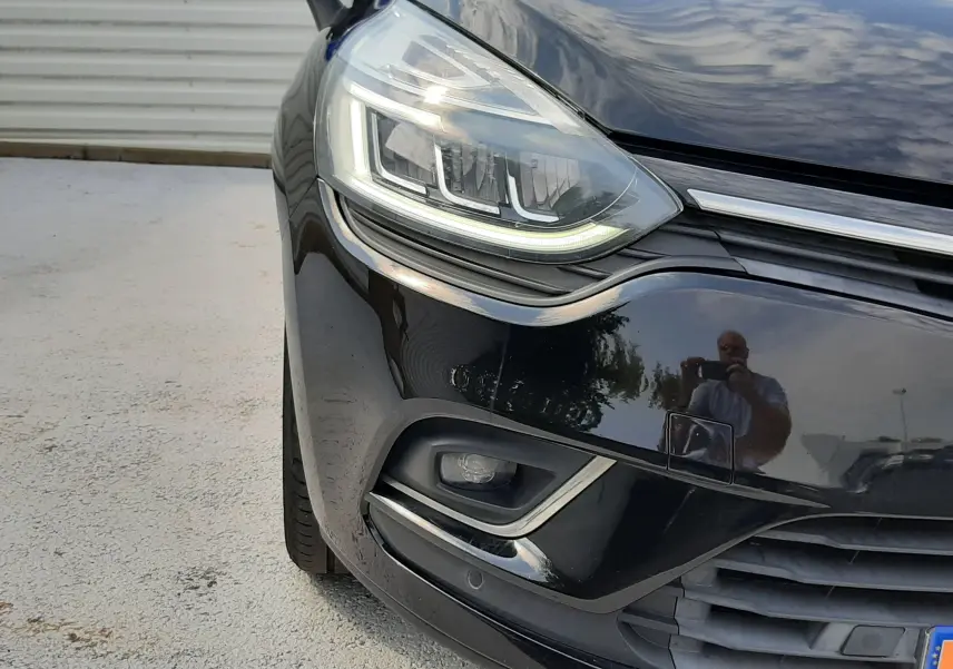 Gros plan sur l'avant gauche noir brillant d'une Renault Clio IV 2018, mettant en valeur son phare LED et le pare-chocs.