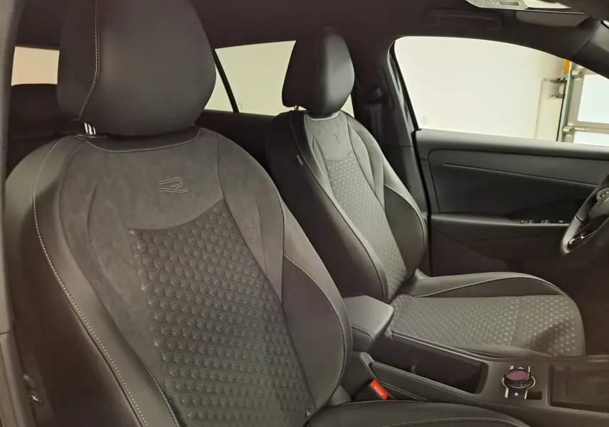 Vue intérieure de profil droit montrant les sièges avant noirs avec surpiqûres blanches et logo R du Volkswagen T-Roc 2026.