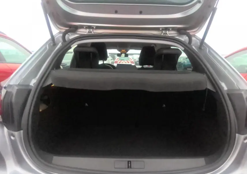 Coffre ouvert vu de l'arrière d'une Peugeot 208 gris clair, montrant l'espace de chargement et l'intérieur sombre.