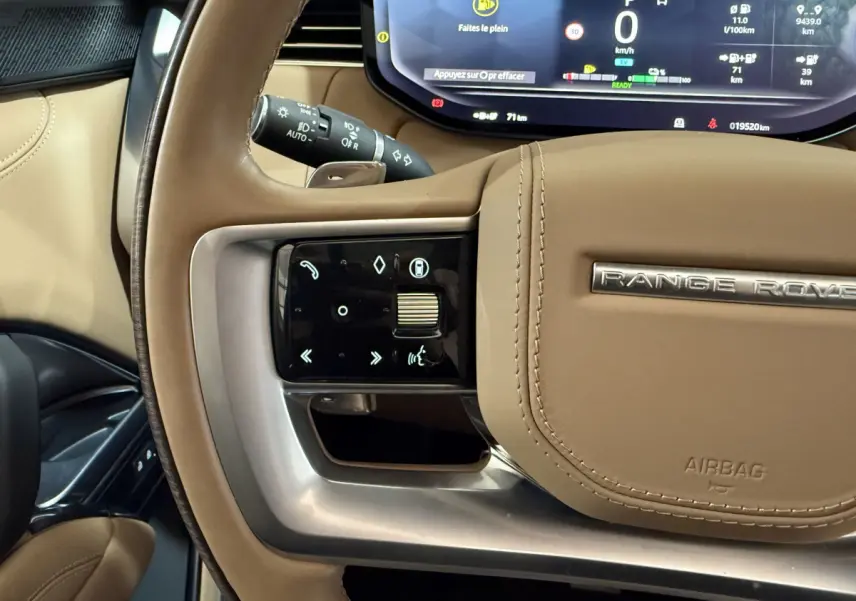 Gros plan sur le volant beige du Range Rover PHEV 2024 avec commandes tactiles et combiné d'instruments numérique visible.