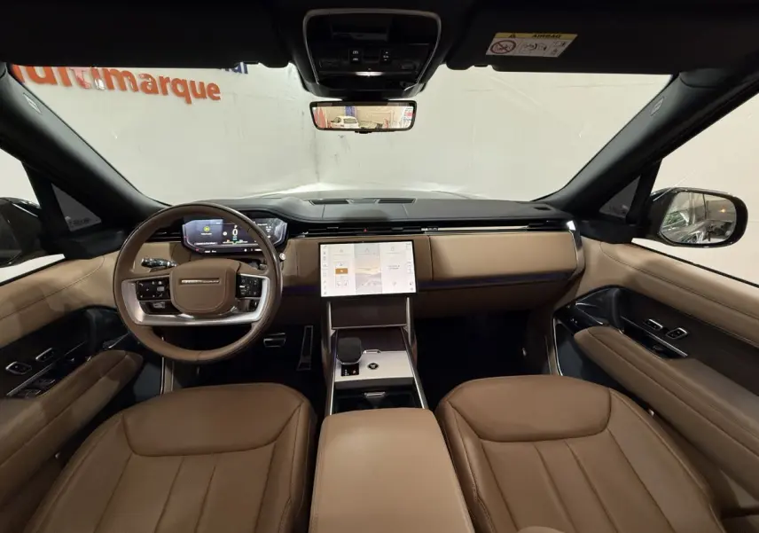 Vue intérieure avant du Range Rover PHEV 2024 avec tableau de bord beige, écran tactile central et volant cuir bois.