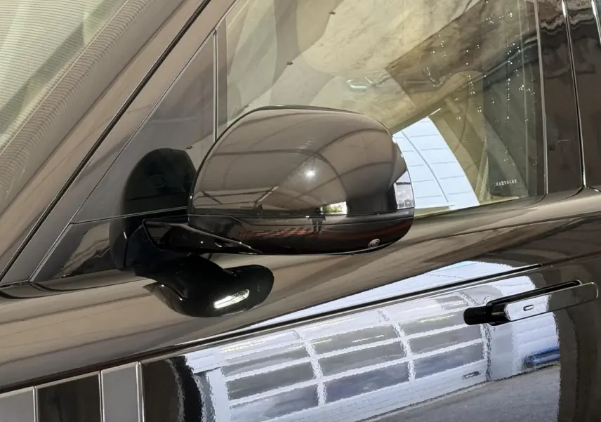 Gros plan sur le rétroviseur rabattable électrique côté gauche d’un Range Rover PHEV noir brillant.