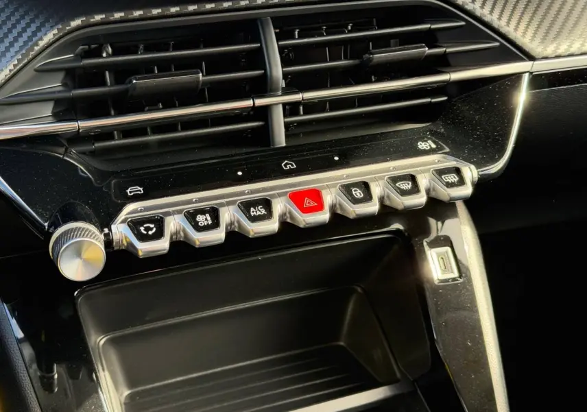Vue rapprochée de la console centrale noire brillante avec boutons de commande et prise USB du Peugeot 208 gris Artense.