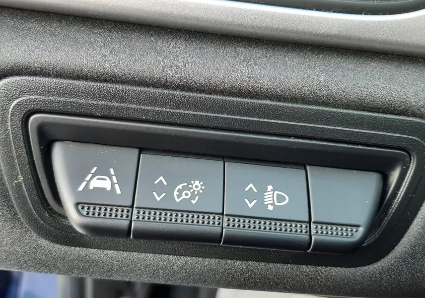Gros plan sur les boutons de réglage d'assistance et d'éclairage du tableau de bord d'un Renault Captur bleu iron toit noir.