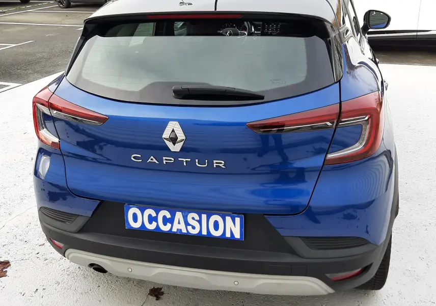 Vue arrière d'un Renault Captur bleu Iron avec toit noir, immatriculé "OCCASION", stationné en extérieur.