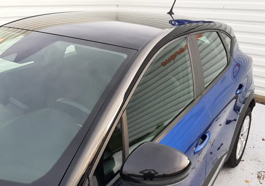 Vue de dessus côté gauche d'un Renault Captur bleu Iron avec toit noir brillant et rétroviseur noir.