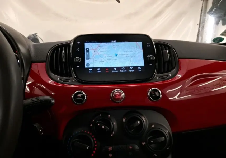 Vue intérieure centrée sur la planche de bord rouge brillante du Fiat 500 Dolcevita avec écran tactile et commandes climatiques.