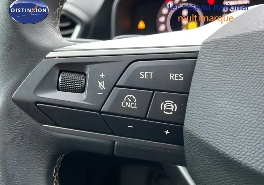 Gros plan sur les commandes au volant à gauche d’une SEAT LEON IV gris fiord, avec régulateur de vitesse et volume.