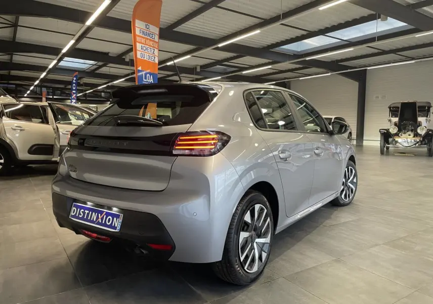 Vue 3/4 arrière droite d'une Peugeot 208 2024 gris clair métallisé avec feux arrière à LED et jantes stylisées.
