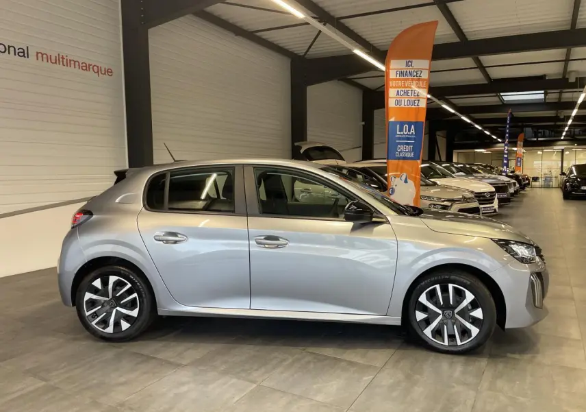 Peugeot 208 gris clair vue de profil côté gauche en intérieur, avec jantes tôle 16'' et rétroviseurs noirs.