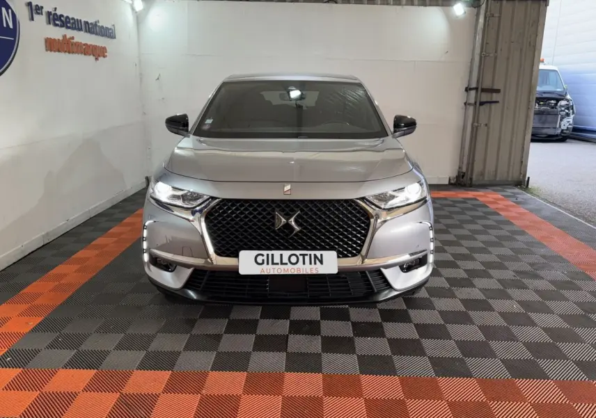Vue frontale d’un DS7 Crossback gris foncé avec calandre noire à motif losange et phares LED allumés, en intérieur.