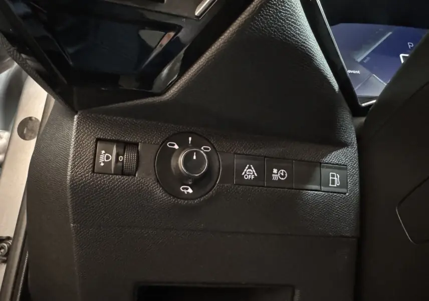 Vue rapprochée du tableau de bord côté gauche du DS7 Crossback gris foncé, montrant les commandes des phares et aides à la conduite.