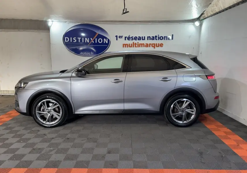 Vue de profil côté gauche d'un DS7 Crossback gris foncé hybride rechargeable garé en intérieur sur sol à damiers noir et orange.