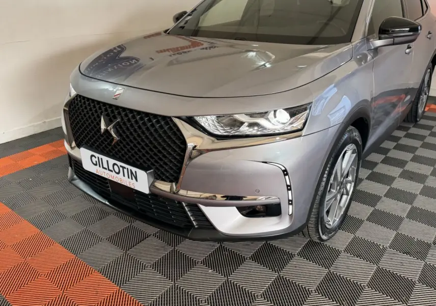 Vue 3/4 avant droit du DS7 Crossback E-TENSE gris foncé avec calandre distinctive et feux LED allumés.