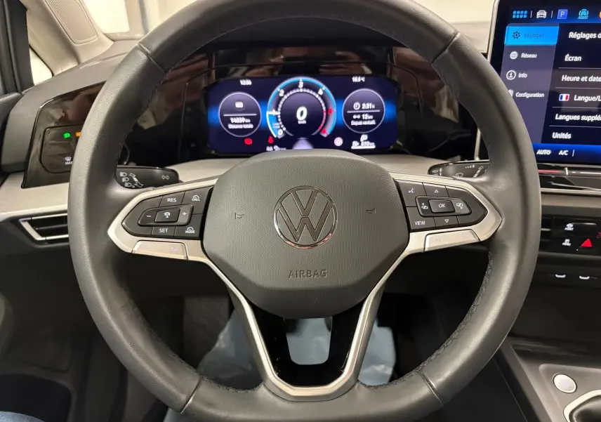Gros plan sur le volant multifonction noir avec logo Volkswagen, tableau de bord digital et écran tactile du Volkswagen Golf 2025.