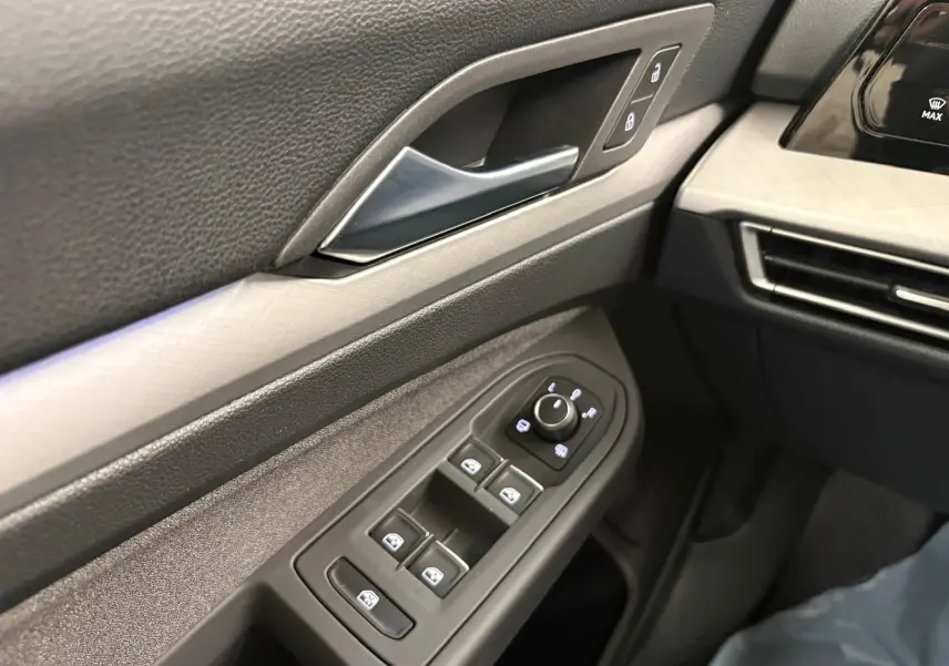 Détail intérieur côté conducteur de la Volkswagen Golf 2025, montrant les commandes des vitres et la poignée de porte en reflet d'argent.