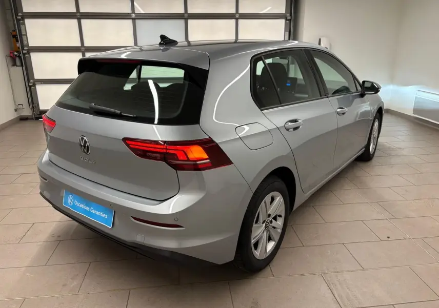 Vue 3/4 arrière droite d'une Volkswagen Golf 2.0 TDI 2025 couleur reflet d'argent avec feux arrière allumés en intérieur.