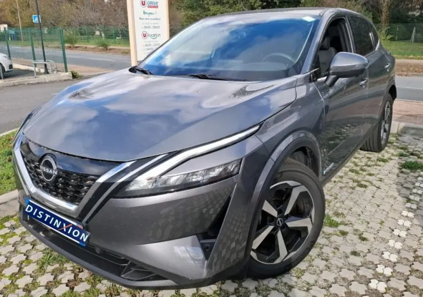 Vue 3/4 avant droit d'un Nissan Qashqai e-POWER gris foncé 2023 avec jantes noires et calandre distinctive.