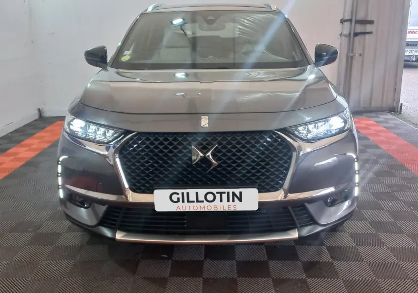 Vue de face du DS7 Crossback gris foncé avec calandre distinctive et feux LED allumés dans un garage.