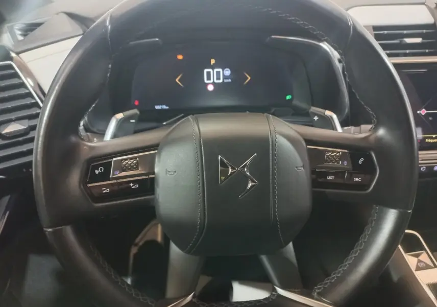 Vue rapprochée du volant cuir noir multifonctions du DS7 Crossback avec tableau de bord numérique en arrière-plan.
