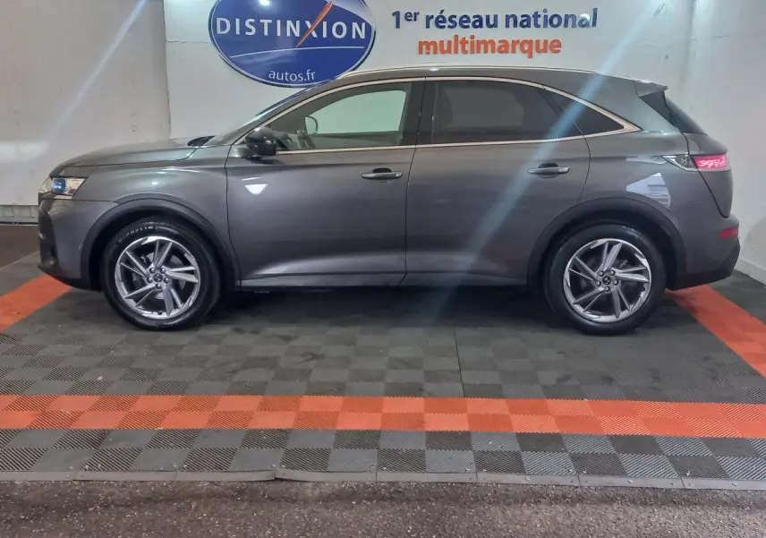 Vue latérale droite d'un DS7 Crossback gris foncé garé en intérieur avec jantes alliage et feux arrière allumés.