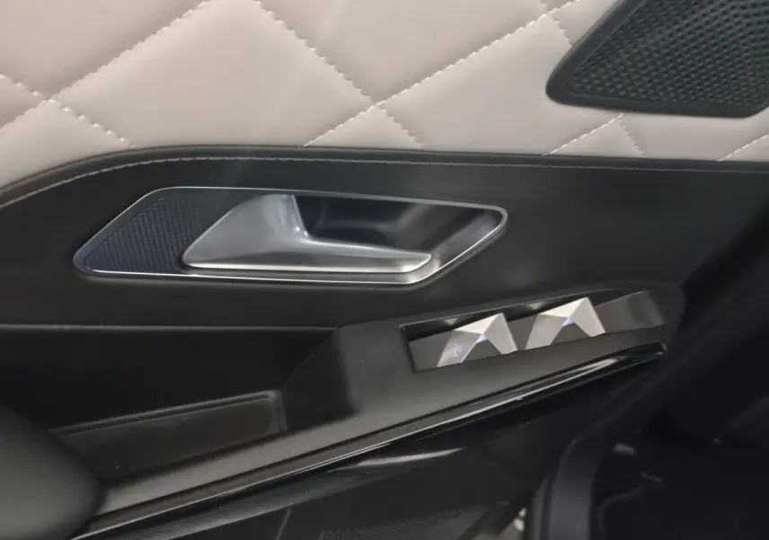 Gros plan sur la poignée intérieure et les commandes de vitre côté gauche du DS7 Crossback gris foncé, finition cuir matelassé.