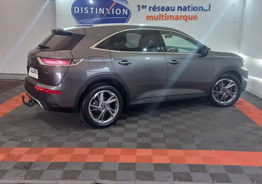 Vue de profil côté gauche du DS7 Crossback gris foncé 2021 avec feux arrière allumés et jantes alliage distinctives.